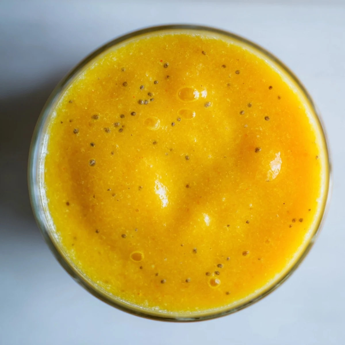 Creamy mango and pineapple protein smoothie recipe garnished with chia seeds in tall glass