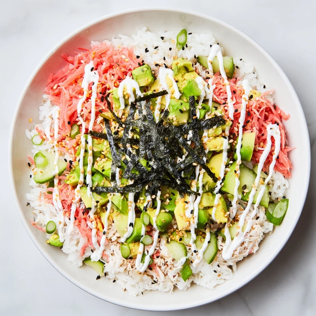 Deconstructed sushi bowl featuring seasoned rice topped with fresh crab, creamy avocado and nori strips