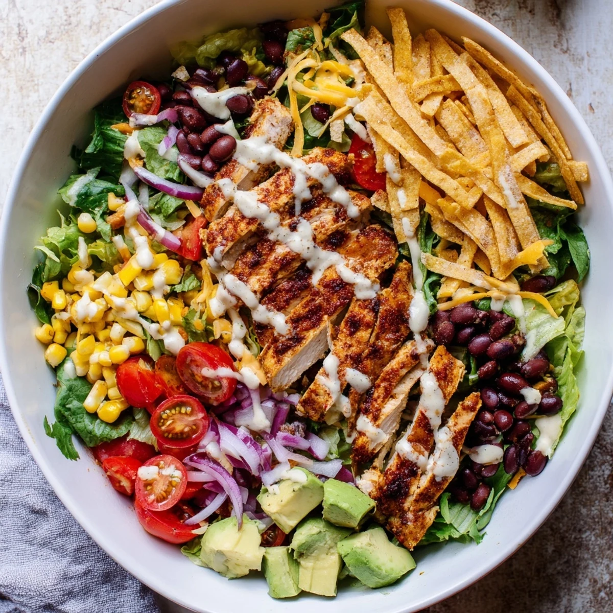 Sliced seasoned grilled chicken resting atop vibrant Southwestern chicken salad with corn, cherry tomatoes, creamy avocado, and zesty lime dressing.