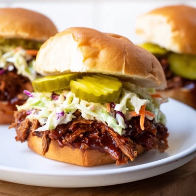 Savory shredded beef brisket sliders featuring tangy coleslaw, crisp pickles, and barbecue sauce, served on toasted buns for game day.