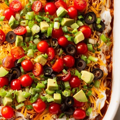 Colorful Ultimate Layered Taco Dip loaded with cheese, avocado, and a side of chips.