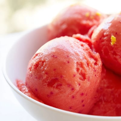 A scoop of tangy Strawberry Lemonade Sorbet glistens with condensation on a spoon.