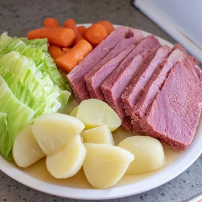 Steaming corned beef and cabbage dinner plated with golden carrots and Yukon Gold potatoes, ideal for a cozy family meal.