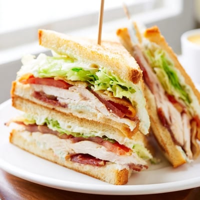 Triple-layered club sandwich featuring juicy tomatoes, golden toast, and creamy mayonnaise spread